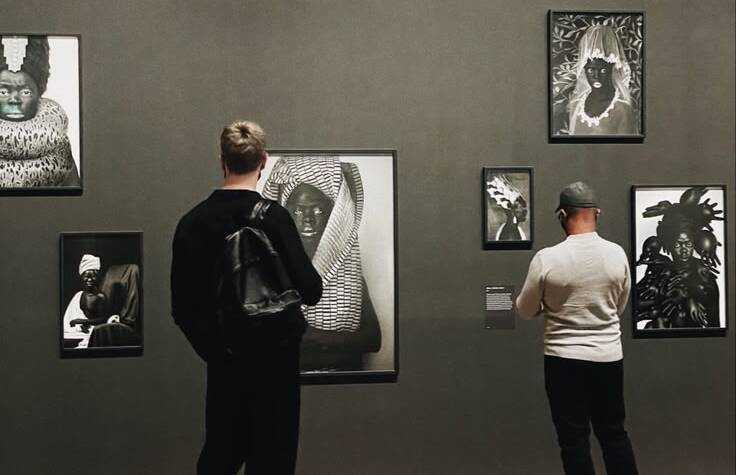 Visitors viewing black-and-white portrait photography in a contemporary gallery space during an Art Exhibition Lahore, with framed artworks displayed on dark walls.