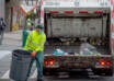 Sanitation worker collecting trash behind a garbage truck on a city street, demonstrating professional Trash removal services kent wa with safety gear and bins.